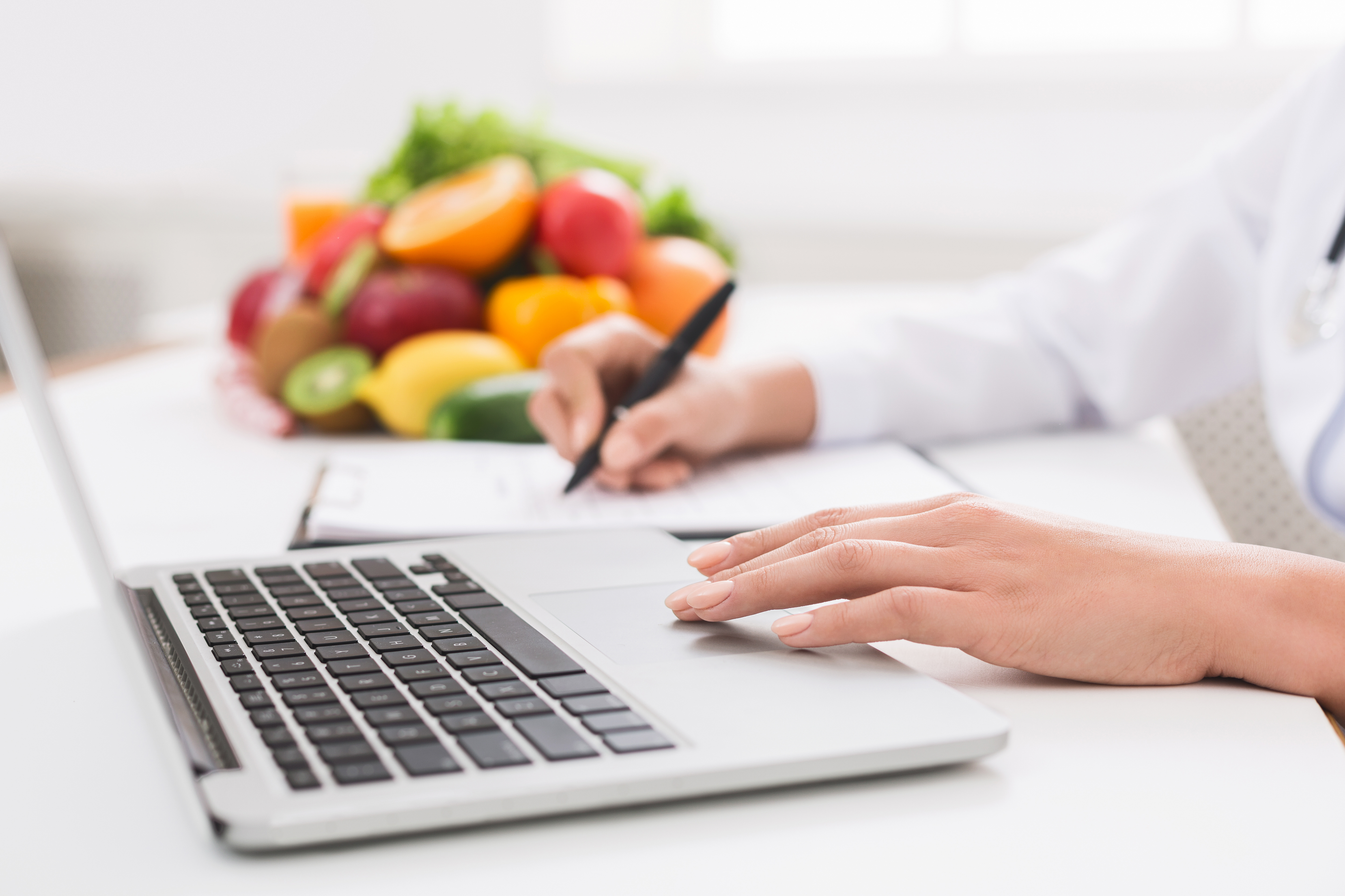 Vrouw zit achter een laptop met een notitieblok en gezonde voeding